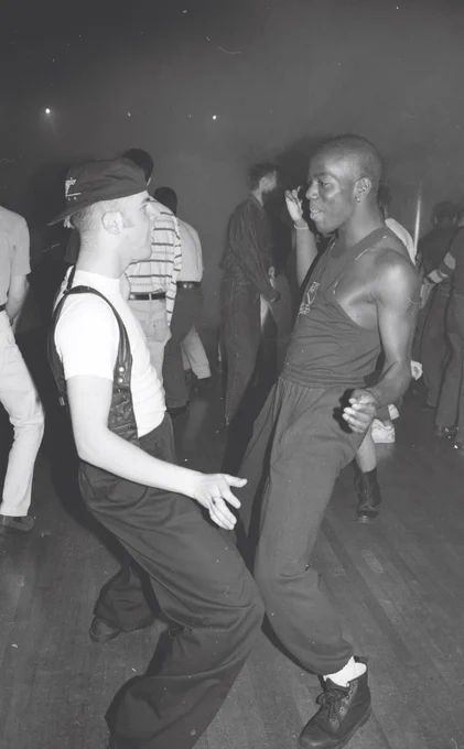A black and white photo of two men dancing in a night club setting