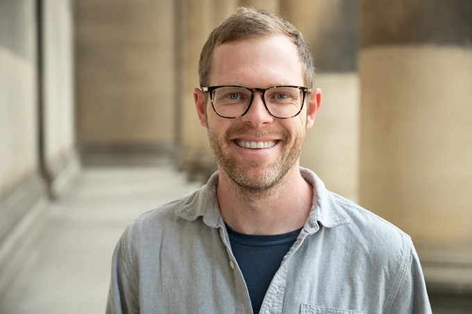 Drew Bridges smiles at the camera as he stands in front of the Mellon Institute's large pillars.