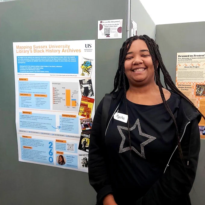University of Sussex Junior Research Associate Myisha Box, standing next to her posted about her project mapping Black Studies in Sussex Library Legacy Collection. 