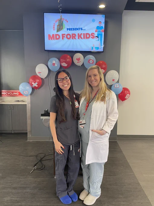 Organizer Tiffany Nguyen and Faculty Tasha Posid pose for a photo in their scrubs in front of an MD For Kids sign.