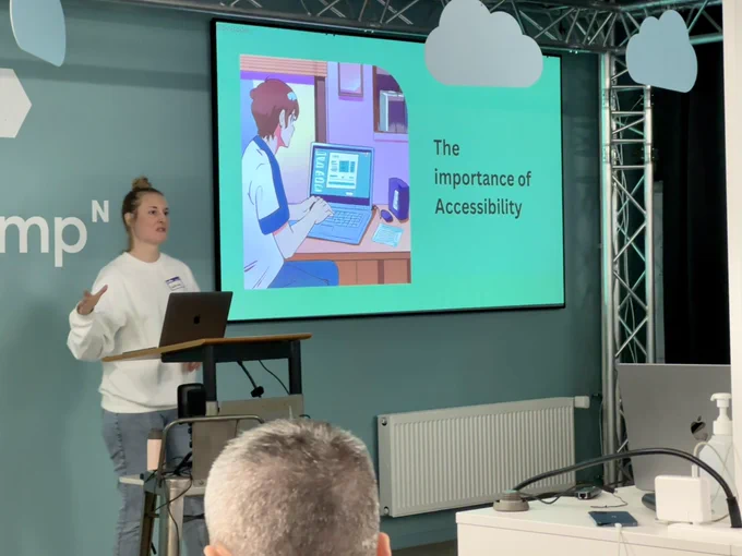 Sabrina on stage giving a talk about accessibility with a slide in the background staring: „The importance of Accessibility“.
