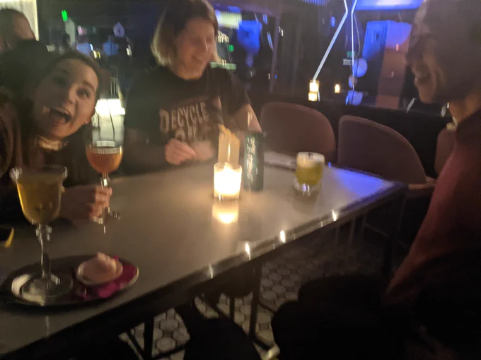 Photo at a dinner table with Laura (smiling happily with her mouth open), JP, and Katy