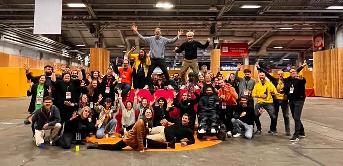 Photo des équipes de CapGame et des interprètes en LSF de Trilogue devant le logo géant #PGW du hall 2.2