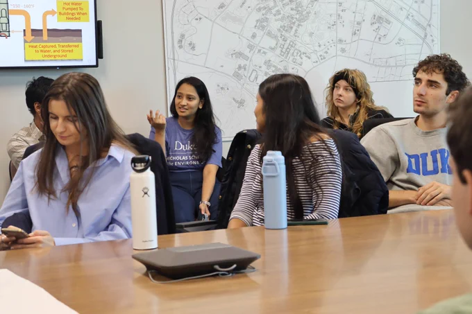 A student asking a question in a group conference room setting.