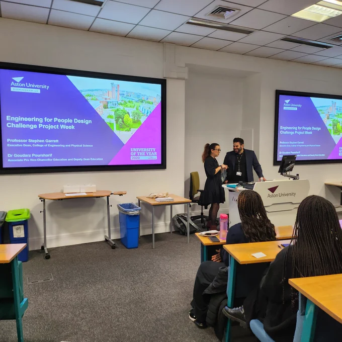 Dr Kyoseva and Dr Poursharif stand in front of the opening slide for the Engineering for People Design Challenge.