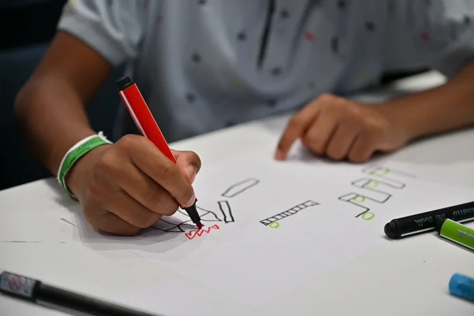 A child draws his own video game level using 4 markers (red, black, blue and green), then photographs and plays it using the Draw Your Game Infinite application.