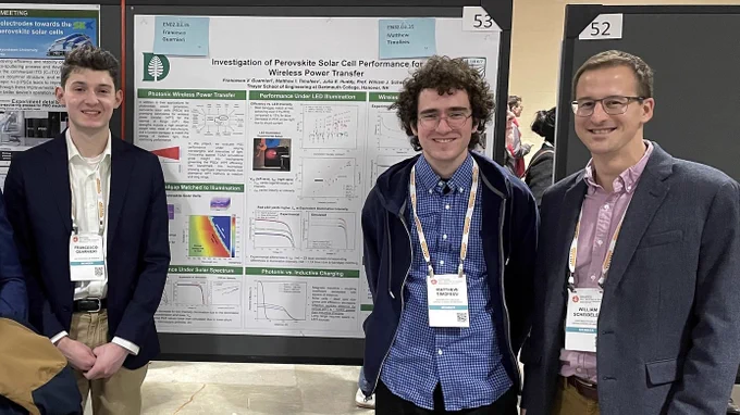 Two students and professor standing in front of a large research poster.