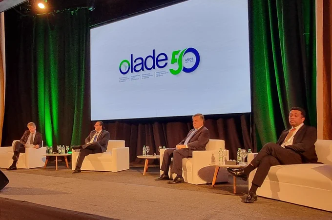 Cuatro hombres en el primer panel, sentados en sillas.  La pantalla dice Olade.