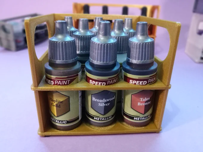 A glittery golden stand with 8 Army Painter small bottles, in 3 rows with 3, 2 and 3 bottles. The three front ones are from the SpeedPaint metallic range: Hoplite Gold, Broadsword Silver and Talos Bronze.