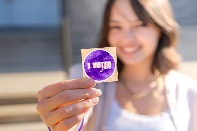 A student holds up an “I voted” sticker.
