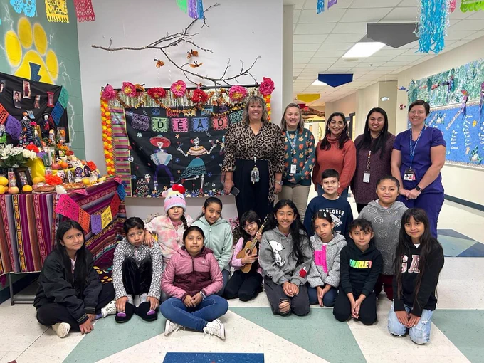 A group photo of about 12 students, two administrators, and three staff members in front of the ofrenda.