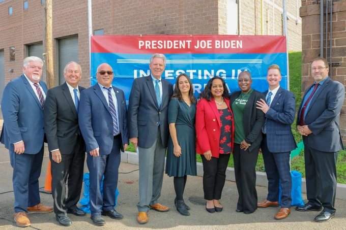 Group photo of event speakers and notable guests standing in front of Investing in America sign.
