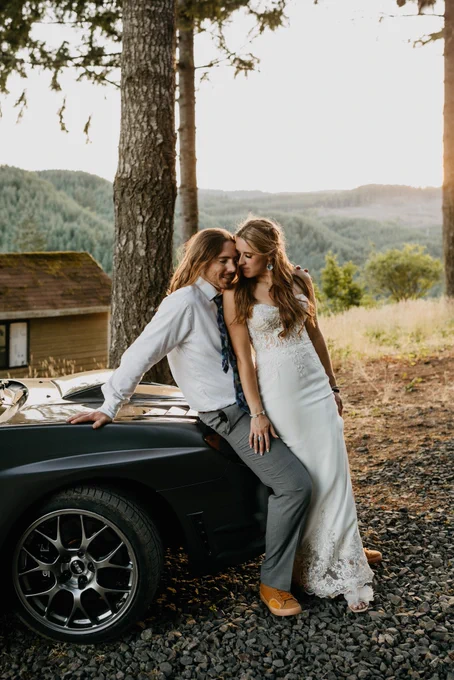 Bride and groom endearingly leaning on a gray sports car