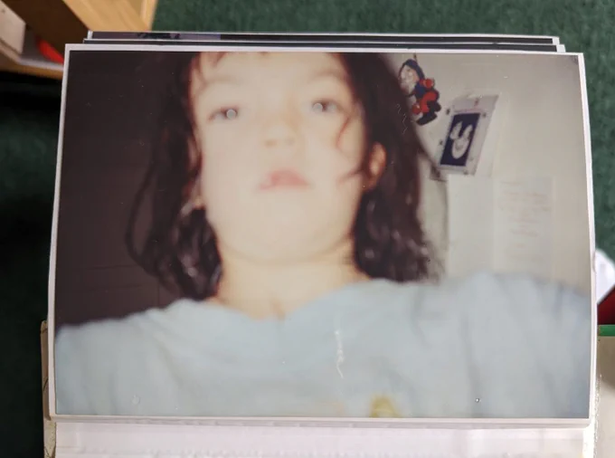 A blurry printed photograph of a young child with long brown hair, pale skin, wearing a light blue t-shirt