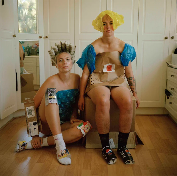 Two androgynous people posing for the camera wearing homemade costumes made of cardboard and plastic bags