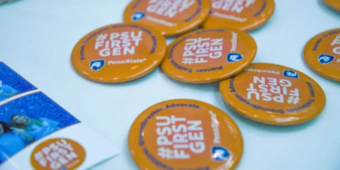 Orange buttons with white #PSUFirstGen text sit on a table at the 2022 event in the HUB-Robeson Center. 