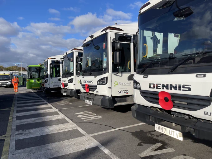 A row of bin lorries with poppies on, photo taken at the dpot with a man in orange work clothes in the background.