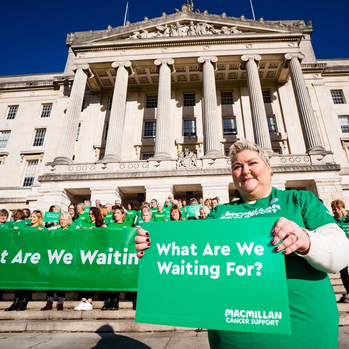 Collen standing outside Stormont holding a sign saying ‘What are we waiting for?’
