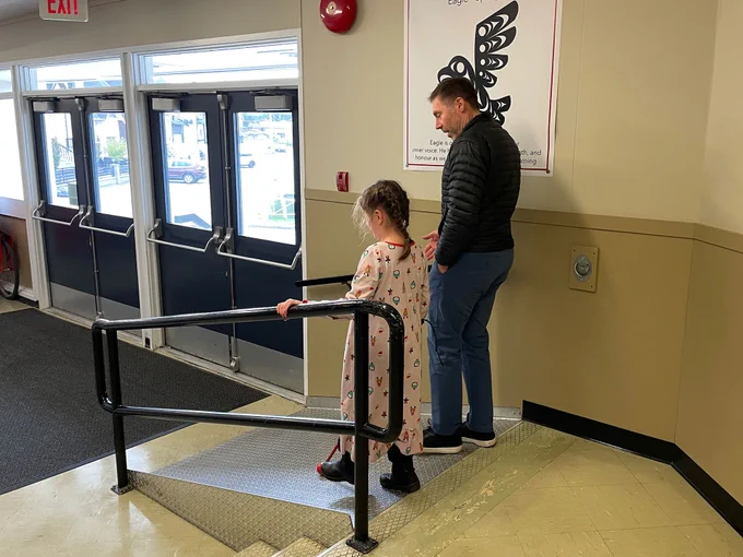A man walking with a girl down a ramp in a school hallway.