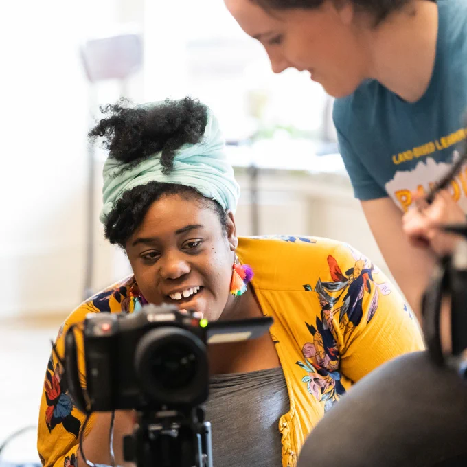A graduate student looking into a camera during a film project.