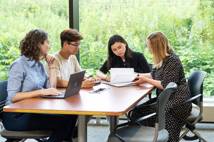 Five people sat around a rectangle table in the library using their laptop and notebook in a collaborative study session. 