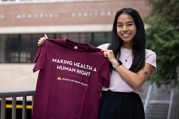 Incoming BA student Tessa Jester holding up a t-shirt that says, "Making Health a Human Right."