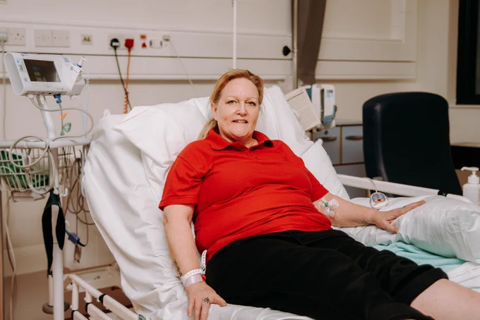 A patient wearing a red polo t-shirt is sitting on a hospital bed preparing to be discharged after a total hip replacement. 