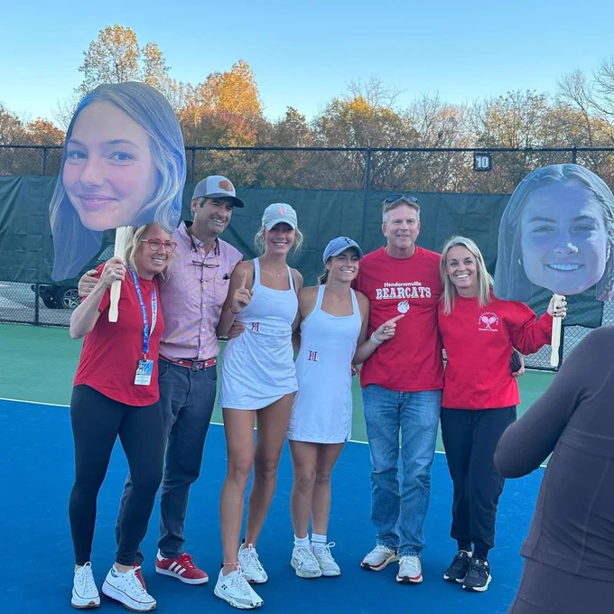Two players posing with their parents that are holding big pictures of their heads on sticks.