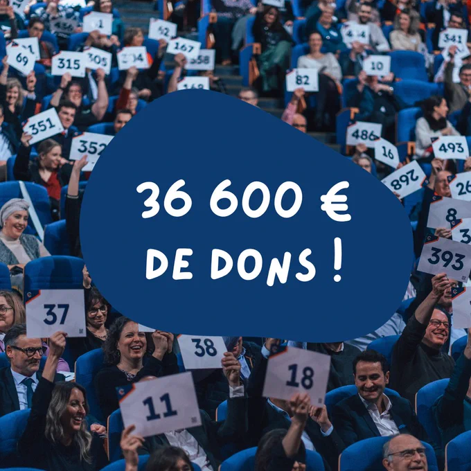 36 600€ de dons ! sur l'image, des centaines de personnes assises dans une salle de spectacle avec des pancartes pour signifier un don d'argent