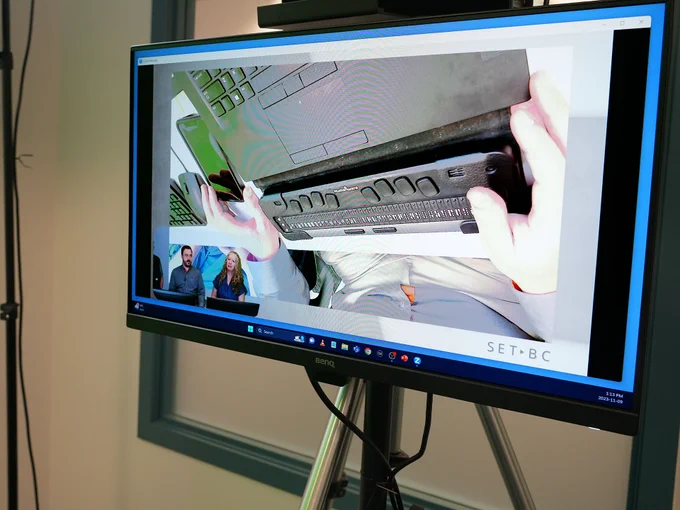 A monitor displaying a close-up of Peter's hands over the Brailliant.