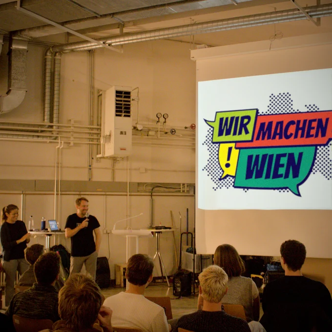 Barbara Laa und Ulrich Leth vor einer Projektion des Logos von Wir machen Wien! Ein Publikum von 7 Personen blickt nach vorne.