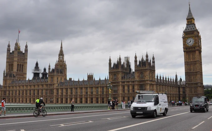 The Houses of Parliament in London, with St Stephen's Tower (home of Big Ben) at the right hand corner. Taken from Westminster Bridge, with pedestrians, cyclists and motorists crossing the bridge.