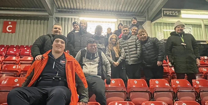 14 Students and staff from the Royal National Collage for the Blind pose for a photo in the red seats of the Merton Stand after yesterday's game. Everyone is wrapped up in coats and hats to keep warm in the cold weather. 