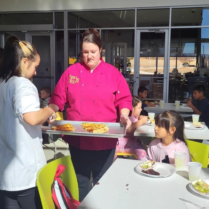 Mrs. Coren and students serving pizza to Dana wildcats sitting at tables.