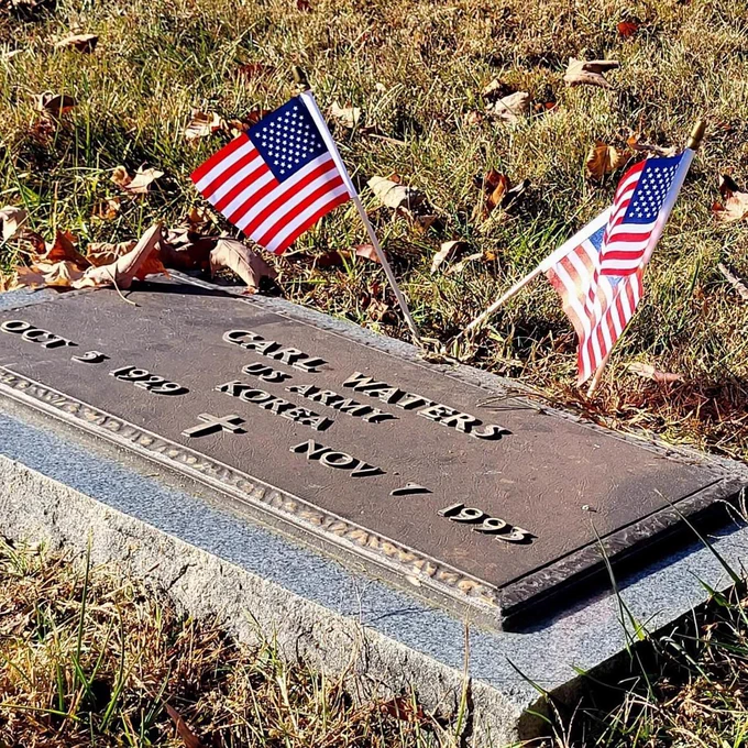 A grave of a veteran with two american flags.