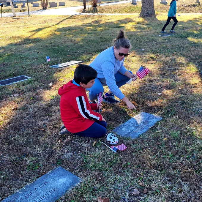 A student and teacher looking at a grave together with flags in their hands.