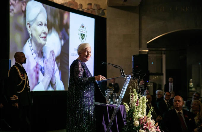 The Lieutenant Governor standing behind a podium on a stage, behind her is a projector image of her photo on a screen