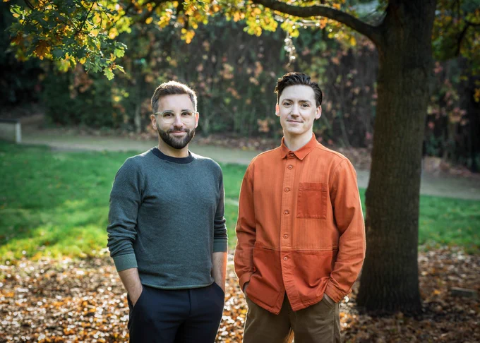 James Pidgeon, Executive Director of Regent's Park Open Air Theatre and Drew McOnie stand together on the theatre lawn smiling.