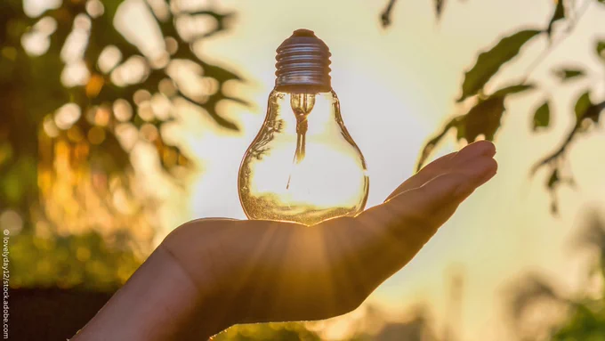 A person holding on their hand a light bulb against sunset in nature.