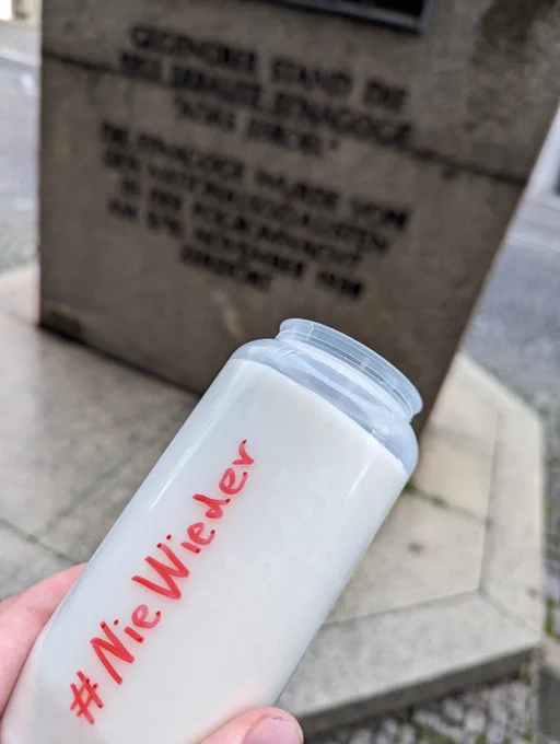 Weißes Grablicht mit roter Handschrift "#NieWieder" im Hintergrund sieht man unscharf das Denkmal zur Adas Jisroel Synagoge in Nürnberg 