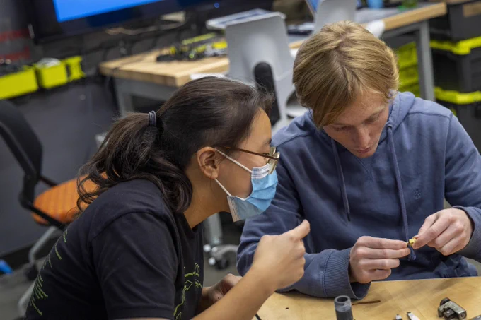 A student shows another student a small piece of hardware at BeAM, UNC's makerspace