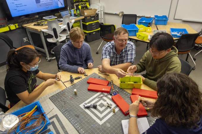 Four students work with a professor to use tools and materials at BeAM, UNC's makerspace. They sit around a small table to collaborate.
