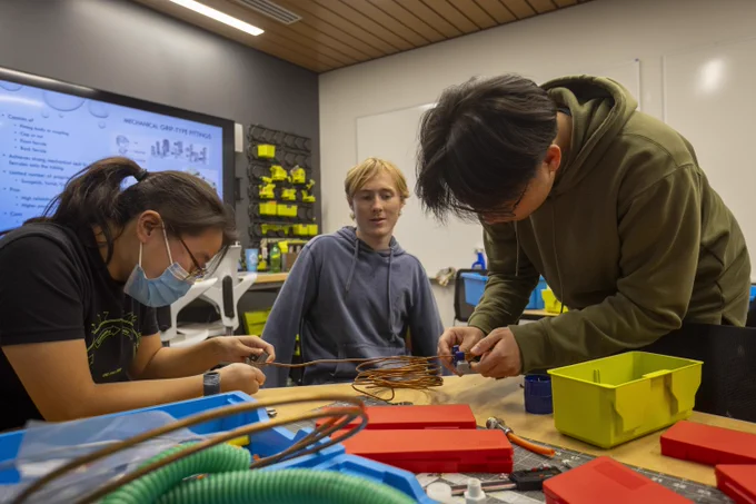 Three students work with wire and hardware at a table at BeAM, UNC's makerspace