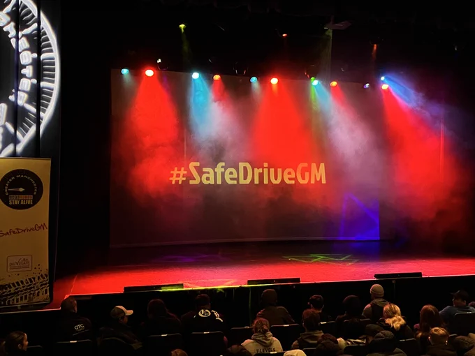 Stage light up with red and blue lights with projector reading, '#SafeDriveGM'