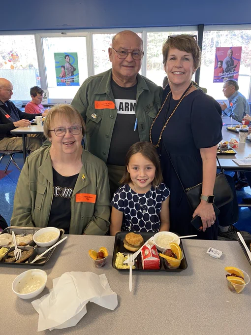 grandmother and grandfather veterans in army shirts and green jackets pose with their daughter in law and granddaughter