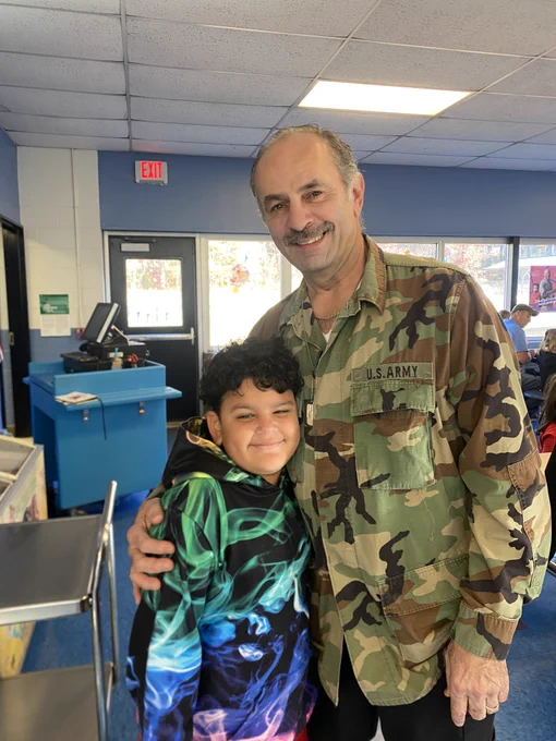 boy and grandfather (dressed in army fatigues) smile at the camera and embrace