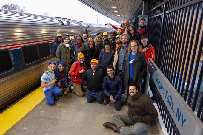 A group of over 20 smiling Wikimedians on a train platform.