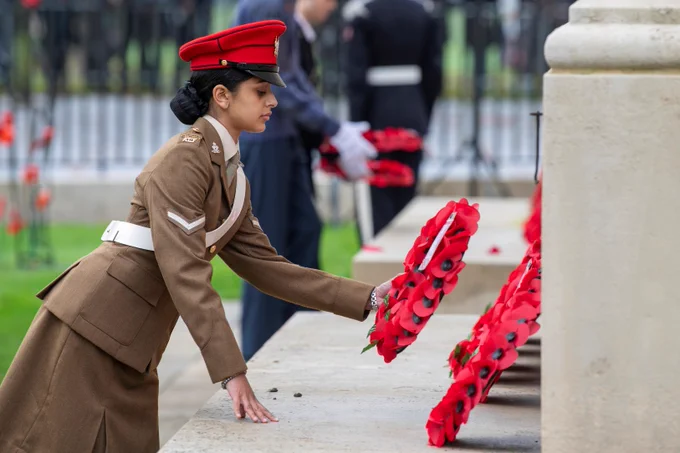 Woman in military uniform leans forward to place a poppy wreath at the War Memorial