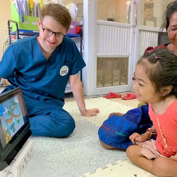 A girl using a eye-gaze system with Charlie nearby and a relative.