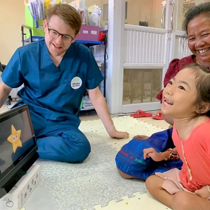 A girl using a eye-gaze system with Charlie nearby and a relative.